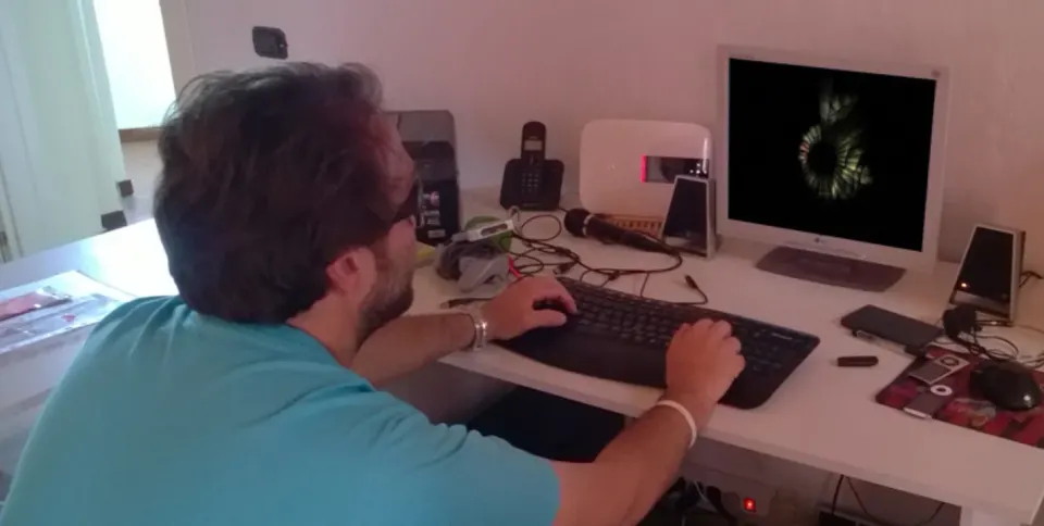 Un jugador probando el juego en un escritorio, con micrófono y altavoces junto a un monitor que muestra una espiral oscura
