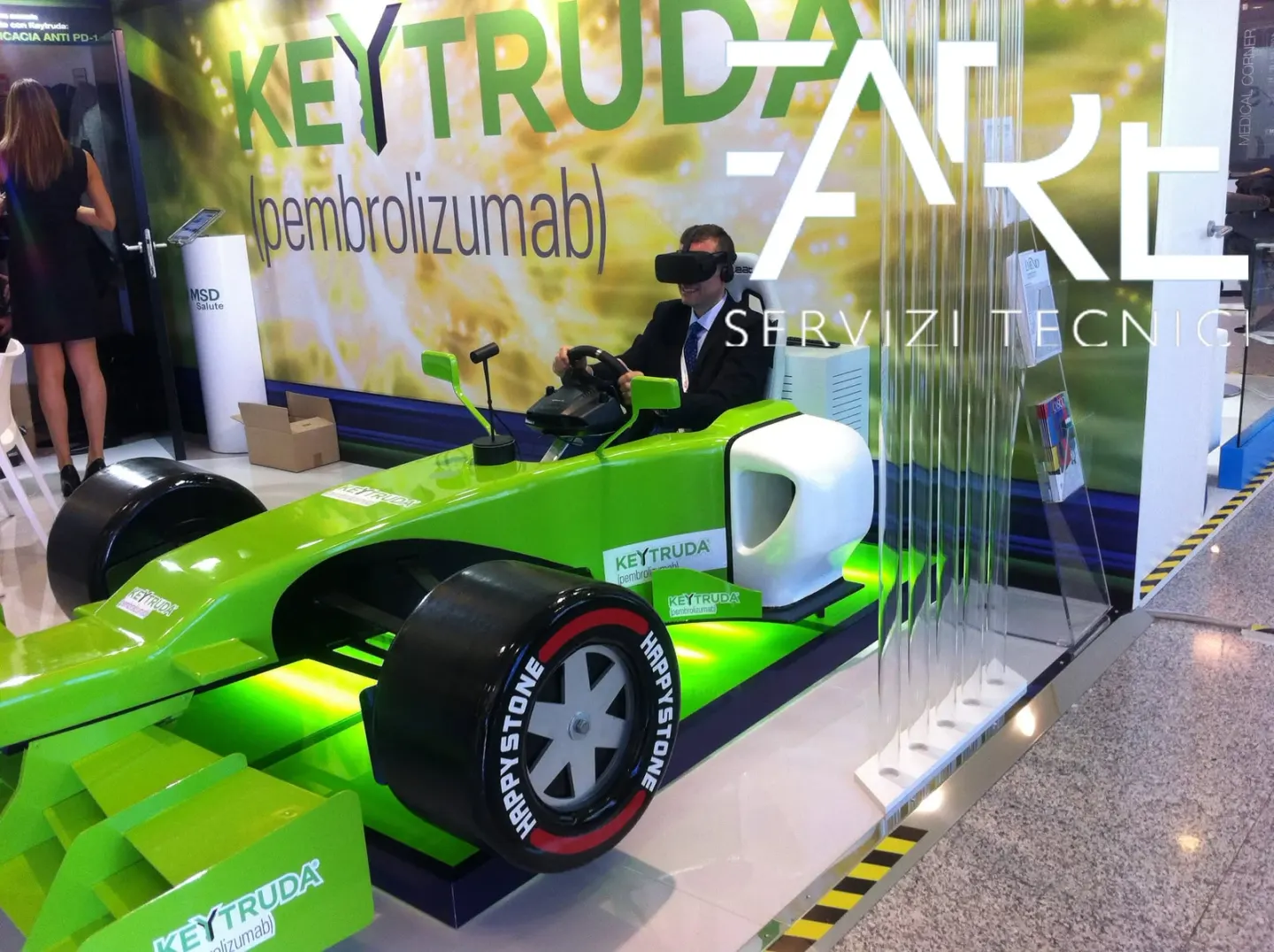 Visitante con visor de realidad virtual sentado en un simulador de monoplaza verde en un stand de evento farmacéutico